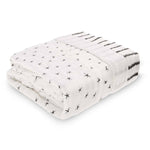 The aden + anais boutique silky soft muslin oversized blanket is crafted from folded white fabric adorned with small black star-like patterns. Its edge boasts a charming black and white striped pattern, offering cozy comfort.