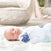 A baby sleeps soundly wrapped in an aden + anais boutique 100% cotton muslin swaddle blanket, featuring blue and teal animal prints. The serene scene is completed by a cozy beige and gray textile backdrop, accented with a calming green plant.