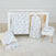 The nursery includes a white crib with wooden slats, featuring aden + anais boutique iconic cotton muslin dream blanket in floral and polka dot patterns. A zip-up baby garment hangs on the crib, while a stool holds folded blankets. A white rug and plush item sit on the beige floor.