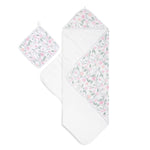 The aden + anais boutique set includes an oversized 100% cotton muslin-backed hooded towel and washcloth, adorned with a floral pattern in soft pink, peach, and green. Both pieces have convenient hanging loops.