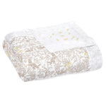 The aden + anais boutique silky soft muslin oversized blanket is perfect for family snuggles, featuring a folded white fabric with a beige floral and leaf design. Yellow and gray abstract dots in the corner add a playful touch to this lightweight bamboo viscose blend.