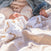 A close-up of a baby’s bare feet on a soft HALO Fall/Winter SleepSack Wearable Blanket Bundle outdoors. The baby wears beige clothes and a denim jacket as sunlight adds a gentle glow to the cozy scene.