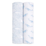 Two rolls of GOTS certified fabric stand upright: one with small blue dots in grids, the other with light blue whales on white. Both are perfect for crafting organic muslin swaddle blankets like those by aden + anais.