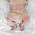 A baby in beige ribbed shorts with a white drawstring and matching top lies comfortably on gray and white elephant-patterned sheets, showcasing their belly button. The bamboo-infused viscose fabric of their outfit ensures silky soft comfort, similar to the aden + anais boutique swaddle blankets.
