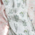 The aden + anais boutique silky soft swaddle blanket 3 pack showcases a close-up of floral patterns with delicate green and pale pink flowers on a light background. The silky fabric gently catches the light, highlighting its intricate design and slightly crumpled texture.