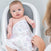 A baby in a gray and white infant bath seat smiles, wrapped in an aden + anais Organic Baby Essentials Bundle blanket with colorful patterns, as an adults hand gently reaches toward them from the right.