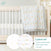 An aden + anais essential set includes a light wooden crib with white bars, draped with a cotton muslin animal-print blanket. It features 100% cotton sheets and a crib skirt. On the image: essentials cotton muslin bedding set 3 pack.
