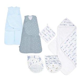 The HALO Bedtime Prep Bundle, featuring sleep sacks, a sleepsack swaddle, organic burpy bibs, and an oversized hooded towel with animal and nature prints in soft blue, white, and gray, is arranged neatly on a white background.