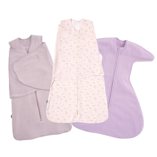 The HALO SleepSack Swaddle Variety Bundle features three swaddles: a solid light purple zip-up, a pink floral pattern for newborns, and a solid lavender swaddle with wide arm flaps and zipper to help your baby sleep soundly.