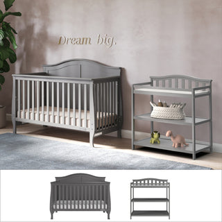 The Child Craft Camden 2-Piece Nursery Set features a gray convertible crib and changing table, arranged against a beige wall with "Dream big." above. The set is styled with green frog and pink dinosaur toys, plus a plant in the corner.