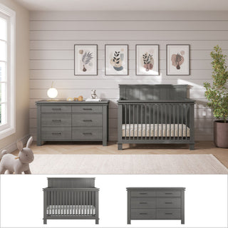 A modern nursery featuring the Child Craft Denman 2-Piece Nursery Set—a gray convertible crib and matching dresser—rests against a white shiplap wall. Four botanical prints hang above, with a plush bunny on the beige carpet by the window.