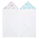 Two essentials cotton muslin hooded baby towels from aden + anais are displayed side by side. The left towel features a pink floral hood, while the right one has a blue and green leaf design. Both white towels are absorbent and folded neatly into triangles.