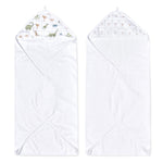 Two white aden + anais essentials cotton muslin hooded towels are shown. The left towel has a dinosaur and palm tree hood pattern, and the right features a subtle small trees pattern. Both boast a triangular hood corner design.