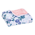 The aden + anais essentials cotton muslin dream blanket, ideal for babies, showcases folded floral patterns with white, blue, and purple flowers. The reverse offers a pink quilted design. Made from soft, absorbent cotton muslin fabric, it ensures warmth and coziness.
