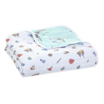 The aden + anais essentials cotton muslin dream blanket, folded white with charming small animal and object illustrations, features soft cotton muslin and reverses to a solid light blue reminiscent of a cozy cloud.