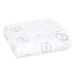 The aden + anais essentials cotton muslin dream blanket is folded and white, featuring a cute rabbit and floral wreath pattern in pastel colors for a cozy, cloud-like feel.