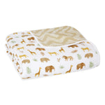The aden + anais essentials cotton muslin dream blanket features a charming pattern of elephants, giraffes, lions, and leaves on a white background. The reverse side displays a beige and white zigzag design, providing cloud-like softness.