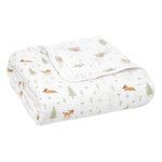 The Disney™ essentials cotton muslin dream blanket by aden + anais is a white quilt featuring a nature-themed pattern with small deer, trees, and delicate leaves in earthy tones. Crafted from soft cotton muslin, its perfect for snuggling and folds to show both patterned and plain sides.