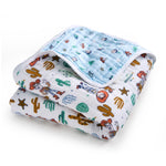 The Disney™ essentials cotton muslin dream blanket by aden + anais is cozy for tummy time, featuring cartoon cowboys, cacti, and stars on a white cotton background. The reverse side is light blue with small cartoon animals and colorful patterns.
