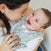 A woman lovingly cradles a smiling baby, wrapped snugly in the aden + anais essentials velboa easy sleep sack 1.5 TOG. They gaze at each other closely, both appearing happy and content.