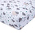 The aden + anais essentials cotton muslin crib sheet features a close-up of a fitted corner, highlighting stylized gray and beige mountains with green and gray trees on white. The soft fabric offers a soothing touch and smooth texture.