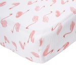 The essentials cotton muslin crib sheet by aden + anais features a playful pattern of stylized pink flamingos in various poses on white fabric, adding a lighthearted touch to the nursery. Made from cotton muslin, the sheet is neatly wrapped and fitted for cribs.
