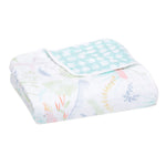 The aden + anais essentials cotton muslin dream blanket features pastel animal illustrations like birds and leaves, with a corner flipped to show cozy light blue polka dots inside. This soft, absorbent blanket is perfect for tender moments with your baby.