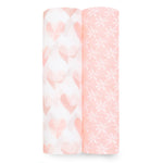 A set of two aden + anais essentials cotton muslin swaddle blankets stands against a white backdrop. One roll features a pink and white heart pattern, while the other showcases a floral design.