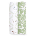 Two vertical fabric rolls display aden + anais designs: a white cotton muslin with rabbit, fox, and badger sketches and a green one with white deer, trees, and house silhouettes. Perfect for essentials cotton muslin swaddle blanket 2 pack.