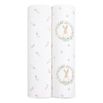 The aden + anais essentials cotton muslin swaddle blanket 2-pack includes two rolled blankets: one with colorful flowers on a white background, and another featuring a rabbit in a floral wreath. Made from soft cotton muslin, they are lightweight and breathable.