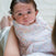 A baby wrapped in an aden + anais essentials cotton muslin swaddle from the 4 pack looks up wide-eyed, with dark hair, cradled by an adult. The breathable fabric ensures comfort as a blurred background highlights the babys expression.