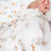 A close-up of a sleeping baby partially covered by an aden + anais Disney™ essentials cotton muslin swaddle blanket featuring delicate animal prints like bunnies and blue butterflies. The babys hand is visible and slightly blurred in the foreground, capturing the essence of these swaddles.