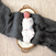 A sleeping baby wrapped in a Disney™ essentials swaddle wrap quick change by aden + anais with pastel patterns lies in a small woven basket on a large gray knitted blanket over a textured beige surface.