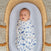 A sleeping baby wrapped in an aden + anais essentials velboa wrap swaddle from the quick change 3 pack TOG 1.5, featuring blue animal patterns, rests in a woven basket on a soft, textured surface.
