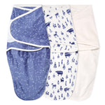 Three aden + anais essentials velboa wrap swaddles are shown: one in dark blue with white constellation patterns, another white with blue abstract animal designs, and a third in velboa minky fabric, plain light cream color.