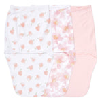 Three baby swaddles are displayed: one with a peach pattern on white, another with a pink floral design, and the third in solid pale pink. Each in aden + anaiss essentials easy swaddle wrap 3 pack has adjustable fasteners for arms-in or arms-out use.