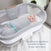 A baby rests in a HALO Swaddle Ideal Temp TOG 1.5, snuggled in gray with IntelliThread for temperature regulation, atop white sheets in a mesh-sided bassinet. Text reads: Swaddle Ideal Temp TOG 1.5 for better, longer, safer sleep.