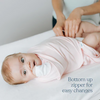 A baby in a light pink outfit has its diaper changed on a table. Text reads: Bottom up zipper for easy changes—perfect with your HALO Eric Carle The Hungry Caterpillar 100% Cotton Swaddle TOG 1.5 or favorite wearable blanket.