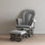 A gray cushioned glider chair with matching ottoman from the Child Craft Hampton Flat Top 3 Piece Nursery Set is placed on a light wooden floor against a plain beige wall. Both pieces feature dark wooden frames finished with baby-safe coatings.