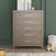 The Child Craft Kieran 3 Piece Nursery Set features a light wood dresser with five drawers and silver handles, positioned against a green wall. A teddy bear and laundry basket sit to the right, while a yellow toy rests on the left, and decorative items adorn the top of the dresser.