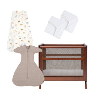 The HALO Mini Crib Essentials Bundle is displayed on a white background, featuring a wooden mini crib with mesh sides, a beige SleepSack Swaddle, an animal-patterned wearable blanket, and two white crib sheets.
