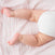 A baby in a white diaper lies on a textured, light pink blanket, with chubby legs and slightly curled feet. The essentials cotton muslin swaddle blanket 4 pack by aden + anais provides breathable cotton fabric and gentle colors, creating a warm and cozy atmosphere.