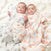Two babies lie on a soft white blanket, each cozy in aden + anais essentials cotton muslin swaddles. One is wrapped in gray zebras, the other in orange tigers. Both look up with curious expressions.