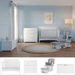 A light blue nursery is furnished with the Child Craft Scout 4 Piece Nursery Set, which includes a white 4-in-1 Convertible Crib, dresser, and toy box. Nearby, a gray glider chair with ottoman provides a cozy seating area, while a round beige rug softens the wooden floor and framed artwork hangs above the crib.