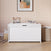 A white Child Craft Scout 4 Piece Nursery Set toy box sits in a room with gingham wallpaper, a framed abstract art piece above, books and an abacus on top, a plush cat toy, and a woven basket to the right—perfectly complementing the crib, dresser, and glider from this cozy and organized nursery furniture set.