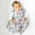 A baby with curly hair, clad in a white long-sleeve shirt and HALOs gray camouflage Wearable Blanket Micro-Fleece TOG 1.0, lies on a white blanket, gazing upwards. This cozy blanket ensures safe sleep with its soft microfleece fabric.