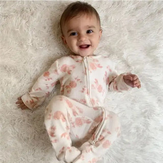 A smiling baby lies on a soft white surface, wearing a cozy onesie—perfect for newborns. The HALO Mini Crib Essentials Bundle provides comfort and style among must-have bedtime essentials.