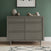 A gray wooden dresser with three drawers from the Child Craft Surrey Hill 2-Piece Nursery Set with Crib and Dresser stands against a green wall, decorated with vases and a wooden toy. Above, a framed abstract artwork is displayed, while part of a patterned rug appears on the floor—creating a cozy nursery setting perfect for pairing with the included 4-in-1 convertible crib or for completing your coordinated nursery ensemble.