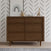 A Child Craft Surrey Hill 2-Piece Nursery Set, featuring a crib and dresser with distinctive angled patterns, stands out against a white wall adorned with black diagonal lines. The top of the dresser displays charming accents—including a framed rainbow print, a plush mouse, books, and a wooden giraffe—that perfectly complement this modern nursery furniture. A rug peeks out from the floor below, tying together the stylish space designed to accommodate your growing child with ease.