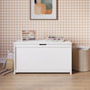 The Child Craft Harmony 33" Kids Toy Box in matte white sits against a brown gingham wallpapered wall, topped with an abacus, books, and framed art. On the wooden floor lie a plush bunny and woven basket, creating a charming, child-safe storage space.